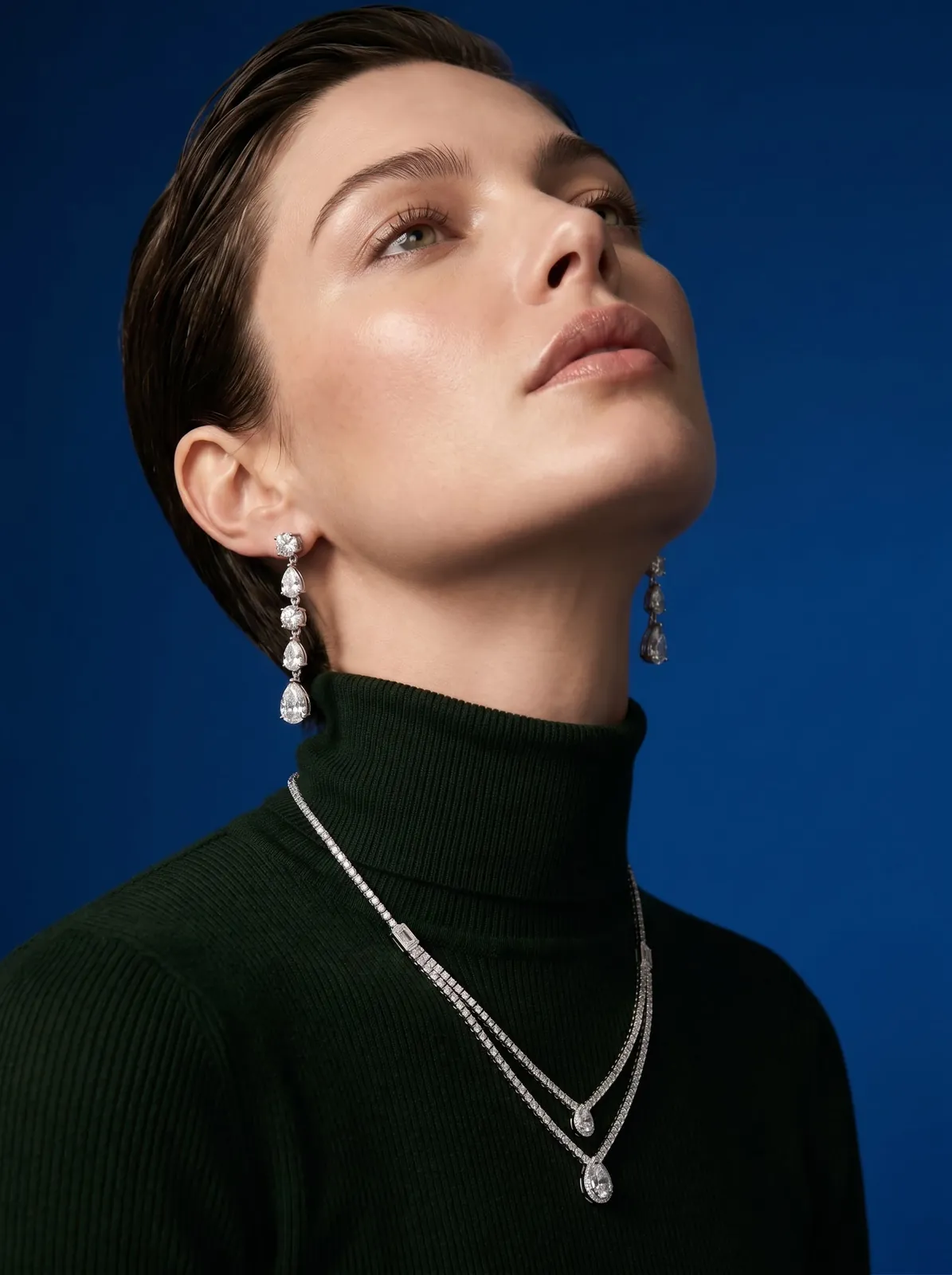 Model in a dark green turtleneck wearing diamond drop earrings and a double-strand diamond necklace, jewelry photography by R2G Studios
