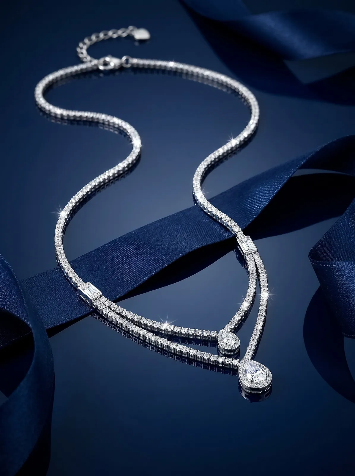 Diamond tennis necklace with pear-shaped drops laid on navy silk ribbon