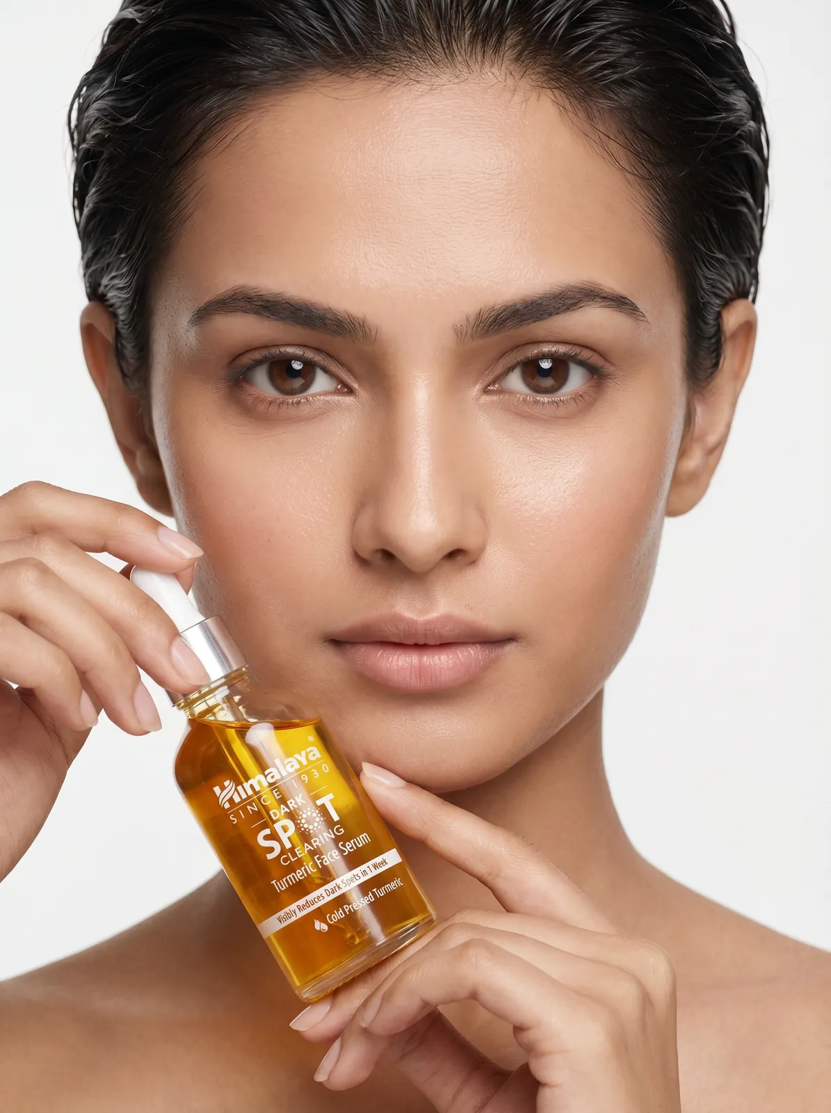 Model holding a face serum bottle next to her cheek, on-model skincare photography