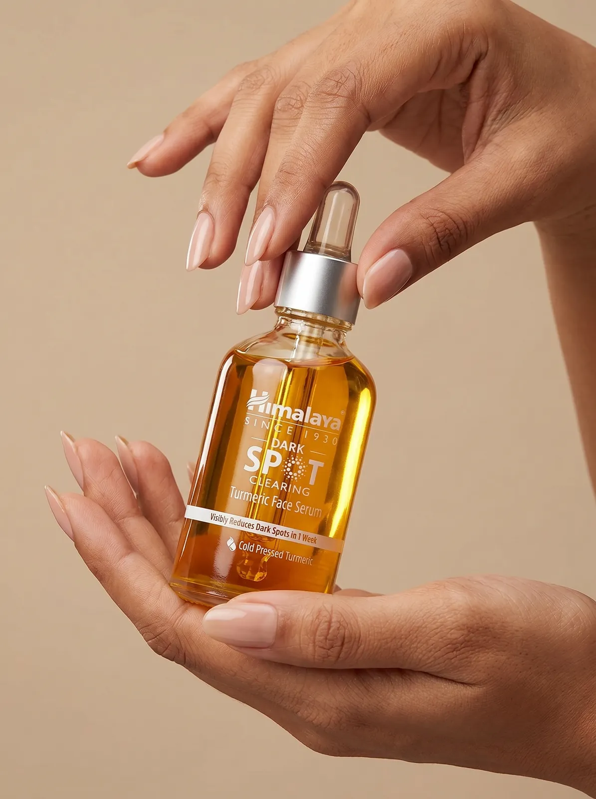 Hands holding a serum bottle against a warm beige background, skincare product in hand